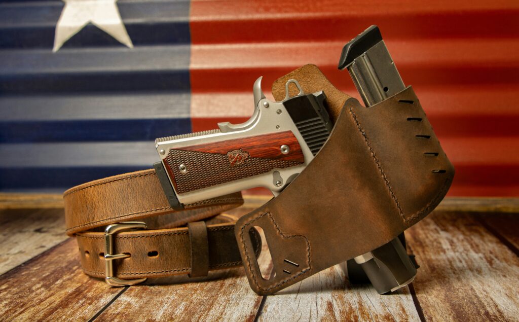 Concealed carry handgun in leather holster with EDC gun belt and magazine against American flag background for firearm training and lawful concealed carry.