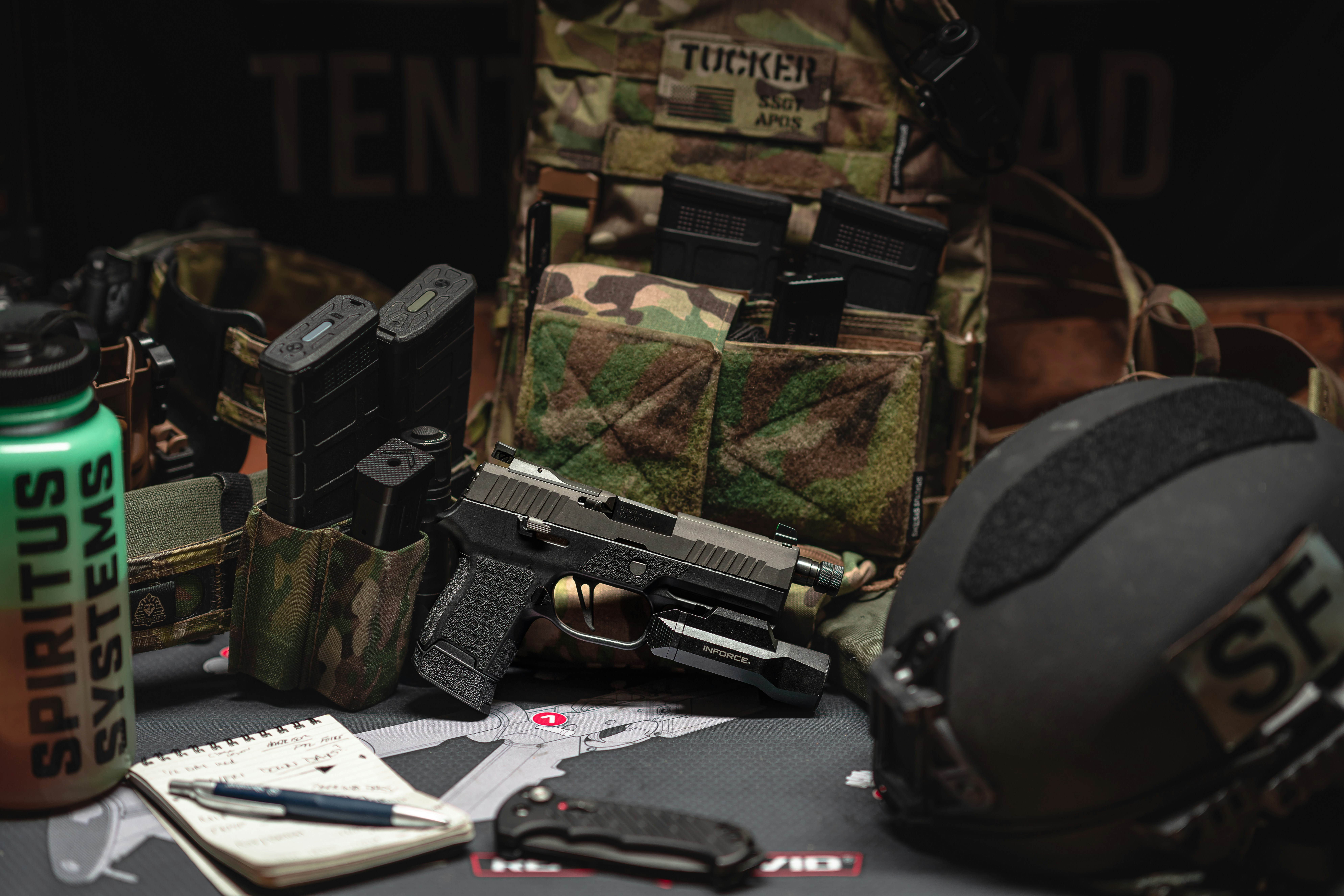 Field attire and tactical gear arranged for training and preparedness, including load-bearing equipment, communications gear, protective equipment, notebooks, and operational field essentials.