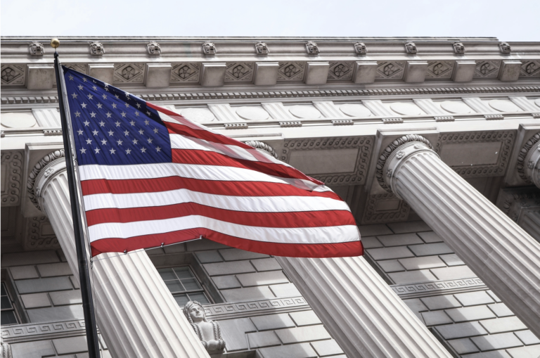 American flag displayed before a building with classical columns, symbolizing constitutional principles, civic responsibility, foundational values, and organizational strength.